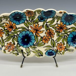 Front view of handcrafted oval ceramic platter with embossed blue and orange floral design and scalloped edges.