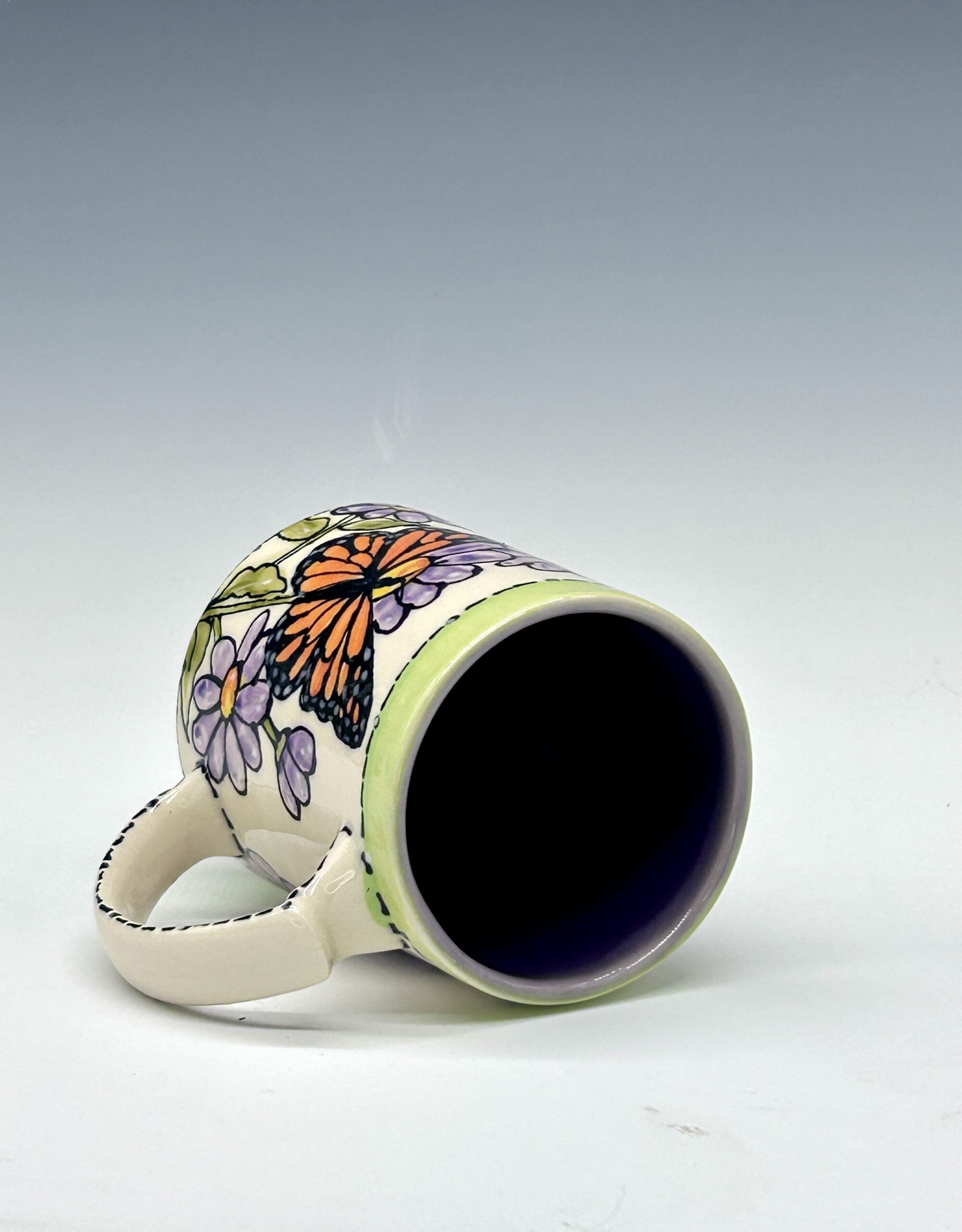 Hand-painted ceramic mug featuring an orange and black butterfly among purple flowers with green accents, view 3