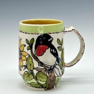 Hand-painted ceramic mug featuring a black, white and red bird among yellow flowers and green leaves, view 0