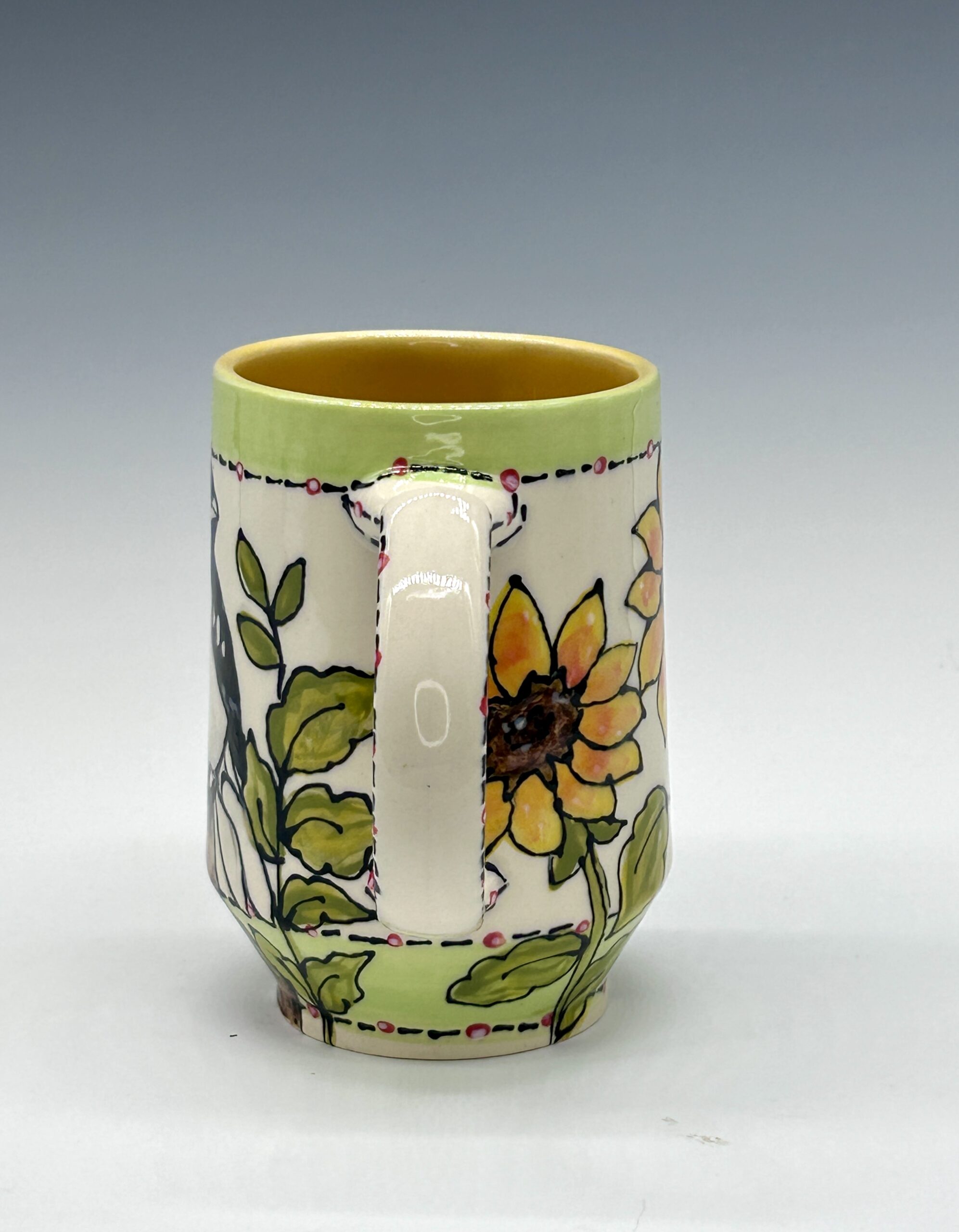 Hand-painted ceramic mug featuring a black, white and red bird among yellow flowers and green leaves, view 2